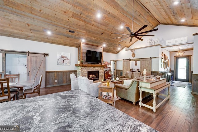 living area with a wainscoted wall, wooden ceiling, a barn door, and a ceiling fan