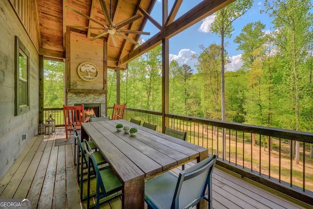 sunroom / solarium with a wooded view, outdoor dining area, a lit fireplace, and ceiling fan