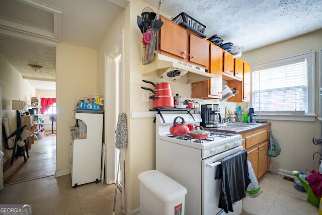 1336 Sharon St NW, Atlanta, GA 30314 - kitchen with a sink, brown cabinetry, white range with gas cooktop, under cabinet range hood, and baseboards