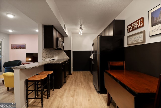 401 N Cromwell Rd Unit 6K, Savannah, GA 31410 - kitchen featuring a peninsula, tasteful backsplash, a kitchen breakfast bar, light wood-style flooring, and appliances with stainless steel finishes
