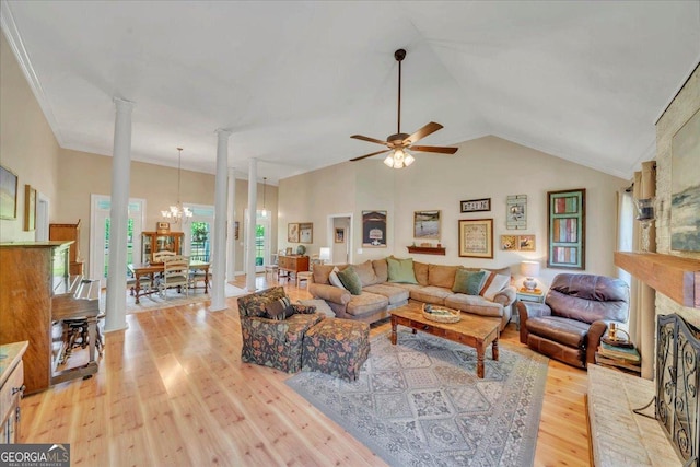 living room featuring ceiling fan with notable chandelier, a brick fireplace, vaulted ceiling, light wood-style floors, and ornate columns