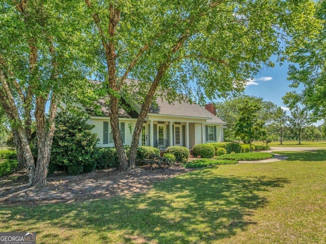 view of front of house featuring covered porch, a front lawn, and a chimney