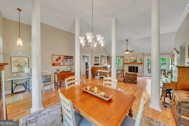 dining space featuring ornate columns, vaulted ceiling, a large fireplace, light wood finished floors, and a ceiling fan