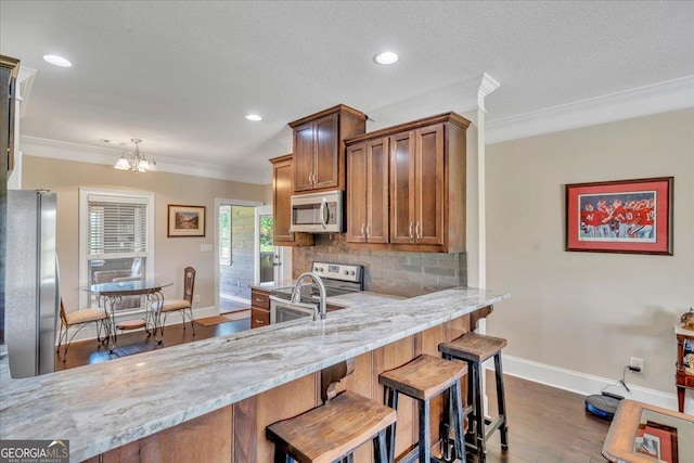 kitchen with stainless steel appliances, ornamental molding, dark wood-type flooring, light stone countertops, and baseboards
