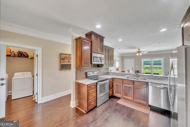 kitchen with ornamental molding, a sink, washer / dryer, stainless steel appliances, and dark wood-style floors