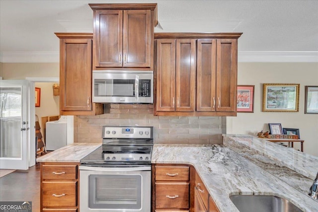 kitchen featuring stainless steel appliances, brown cabinetry, crown molding, backsplash, and light stone countertops