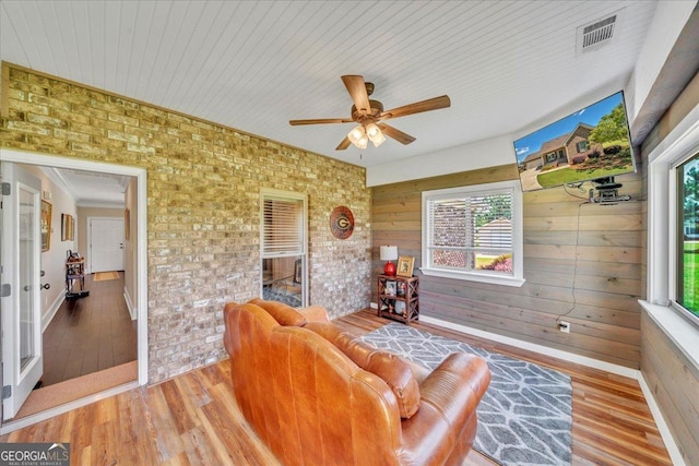 living room featuring wood finished floors, brick wall, visible vents, ceiling fan, and wooden walls