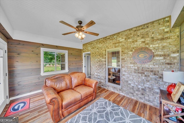 living area with wooden walls, brick wall, ceiling fan, and wood finished floors
