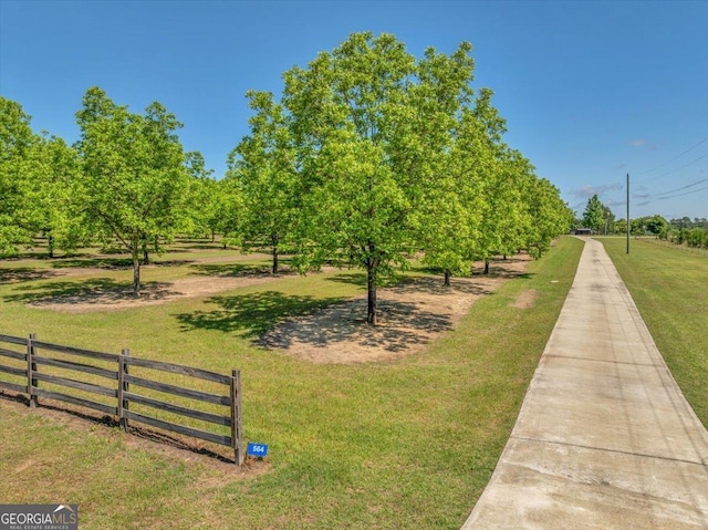 view of community featuring a lawn, a rural view, and fence