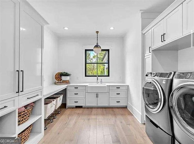 laundry room featuring independent washer and dryer, baseboards, a sink, light wood-type flooring, and cabinet space