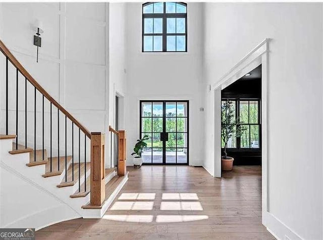doorway with a wealth of natural light, stairway, a towering ceiling, and wood finished floors