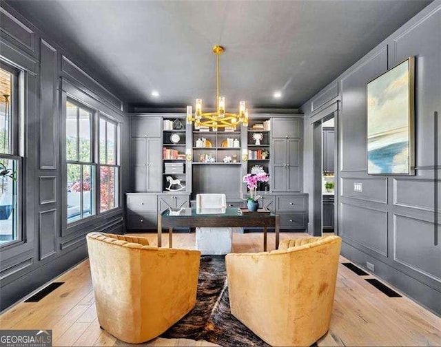 office area featuring a decorative wall, light wood-type flooring, a notable chandelier, and visible vents