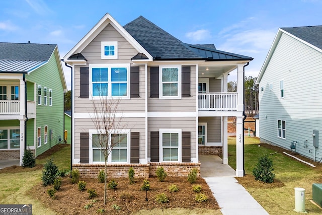view of front facade featuring roof with shingles, a front yard, brick siding, and a balcony