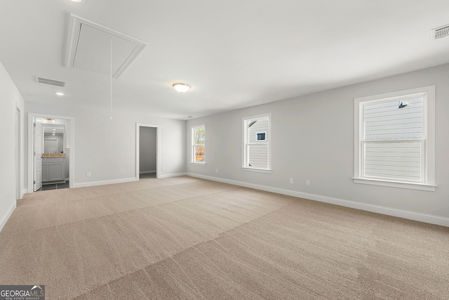 unfurnished living room with attic access, visible vents, baseboards, and light carpet