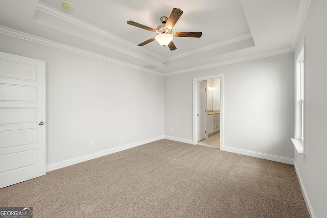 unfurnished bedroom featuring baseboards, ornamental molding, ensuite bathroom, a raised ceiling, and light colored carpet