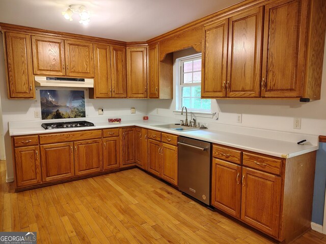 kitchen featuring under cabinet range hood, stainless steel dishwasher, brown cabinetry, and a sink