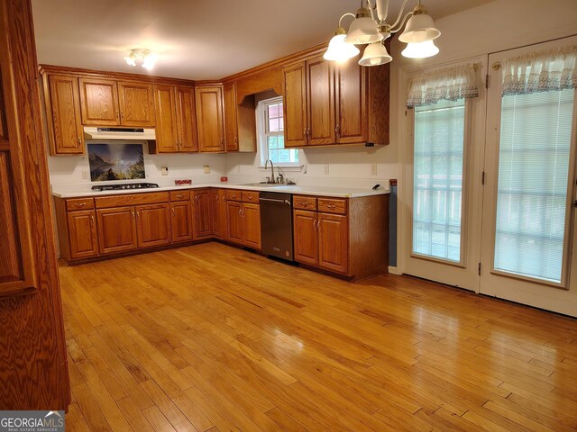 kitchen with a sink, brown cabinets, dishwasher, under cabinet range hood, and a chandelier