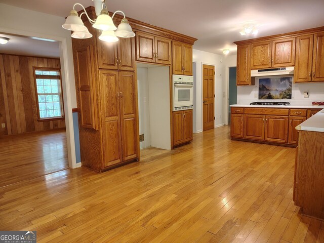 kitchen featuring a notable chandelier, brown cabinetry, gas cooktop, light wood-type flooring, and oven