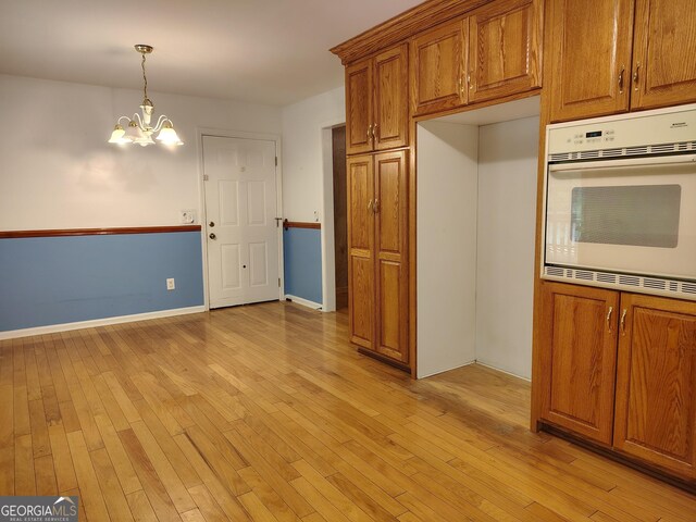 kitchen with brown cabinetry, light wood-style floors, a chandelier, and white oven