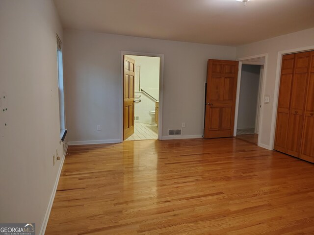 unfurnished bedroom featuring baseboards, ensuite bathroom, light wood-style flooring, and visible vents