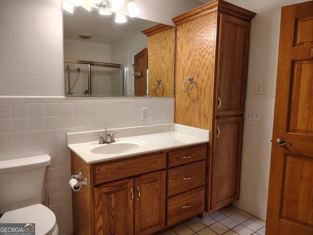 full bathroom with tile walls, toilet, vanity, a stall shower, and tile patterned flooring