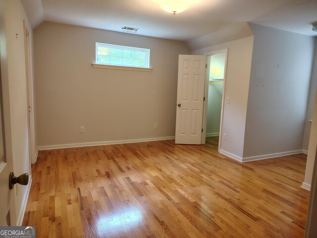 unfurnished bedroom featuring lofted ceiling, baseboards, light wood-style flooring, and visible vents