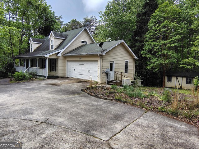 cape cod home featuring a storage shed, covered porch, an attached garage, concrete driveway, and an outbuilding