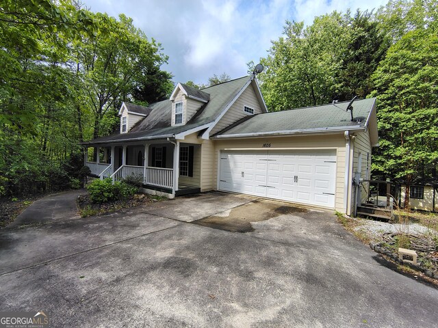 cape cod house featuring covered porch, roof with shingles, an attached garage, and aphalt driveway