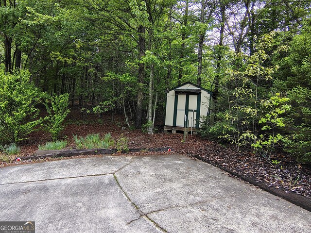view of patio with a storage unit, a wooded view, and an outbuilding