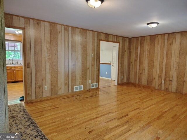 unfurnished room featuring light wood-type flooring, visible vents, wooden walls, and a sink