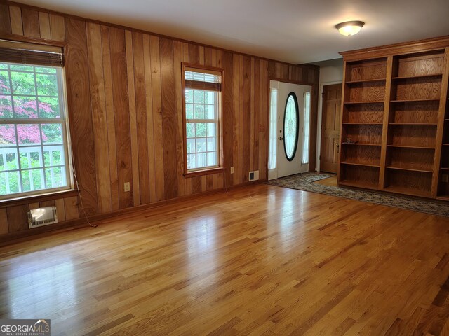 unfurnished living room with wooden walls, visible vents, and wood finished floors