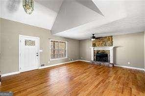 unfurnished living room featuring lofted ceiling, baseboards, a stone fireplace, ceiling fan, and wood finished floors