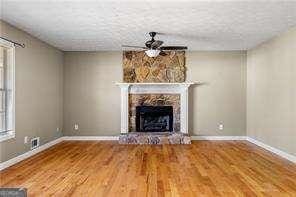 unfurnished living room featuring a textured ceiling, baseboards, a stone fireplace, and wood finished floors