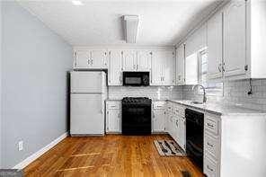 kitchen featuring white cabinets, dark wood finished floors, black appliances, light countertops, and decorative backsplash