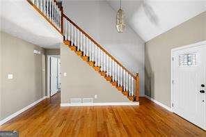 entryway featuring vaulted ceiling, stairway, wood finished floors, and baseboards