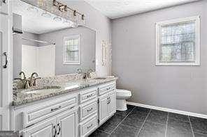 bathroom with toilet, baseboards, double vanity, and a sink