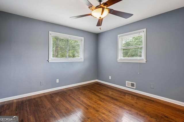 empty room with baseboards, visible vents, a ceiling fan, and dark wood-type flooring