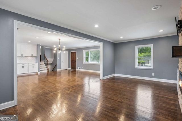 unfurnished living room with an inviting chandelier, a fireplace, crown molding, stairway, and baseboards