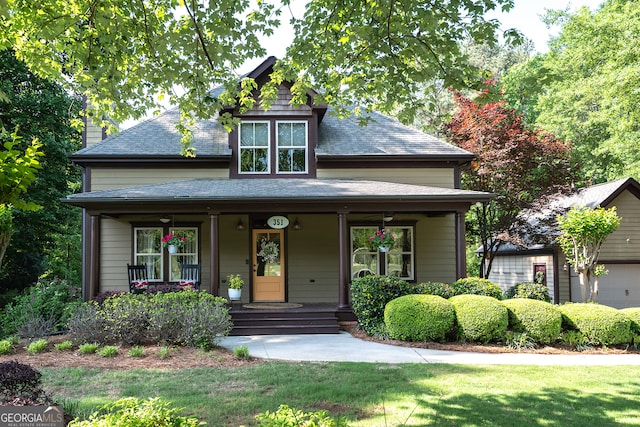 view of front facade featuring a front lawn, a shingled roof, and a porch