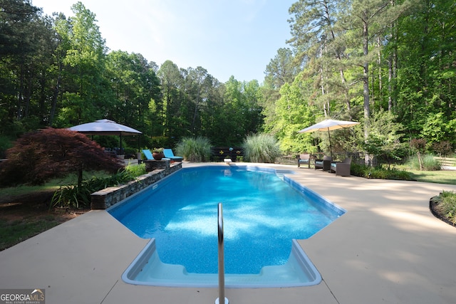 outdoor pool with a patio area and a wooded view