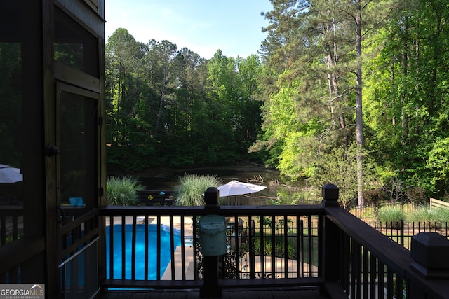 wooden deck with a water view, a view of trees, and a fenced in pool