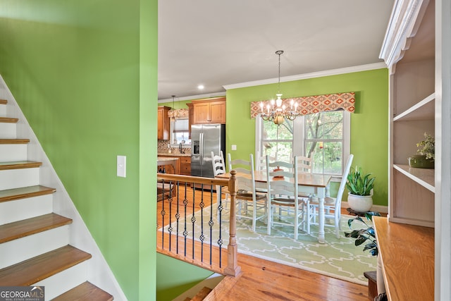dining space with crown molding, light wood-type flooring, an inviting chandelier, and stairs
