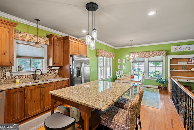 kitchen featuring light wood finished floors, an inviting chandelier, a sink, brown cabinets, and appliances with stainless steel finishes
