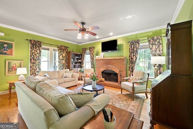 living area with a ceiling fan, a brick fireplace, a healthy amount of sunlight, and crown molding