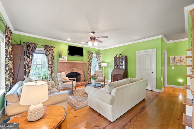 living room featuring a ceiling fan, baseboards, a brick fireplace, crown molding, and hardwood / wood-style flooring