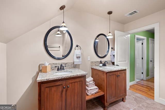 bathroom with two vanities, lofted ceiling, visible vents, and a sink