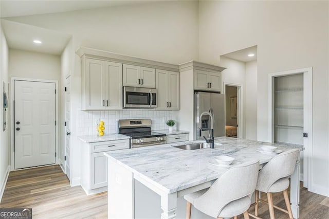 2621 Oldknow Dr NW, Atlanta, GA 30318 - kitchen featuring a sink, light wood-type flooring, a center island with sink, backsplash, and appliances with stainless steel finishes