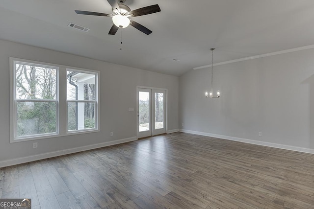 spare room featuring lofted ceiling, ceiling fan with notable chandelier, wood finished floors, visible vents, and baseboards