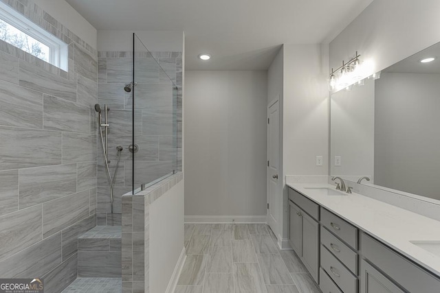 full bathroom with walk in shower, double vanity, baseboards, and a sink