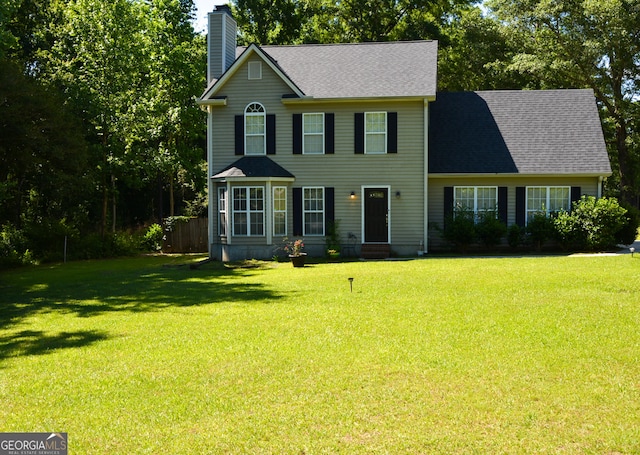 colonial home with roof with shingles, fence, a chimney, and a front yard